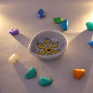 Hand-painted blue pottery diya with floral design surrounded by colorful decorative stones in natural light.