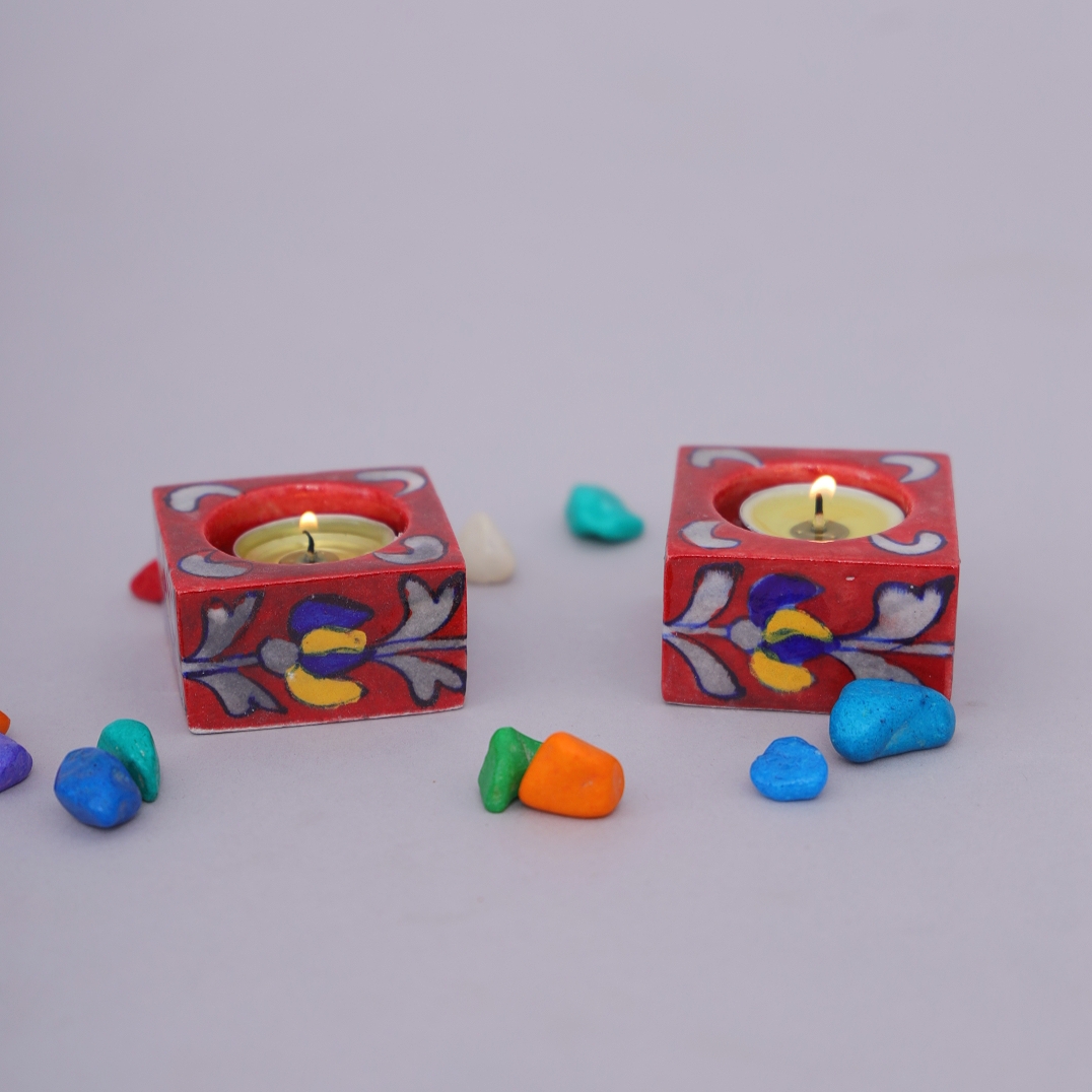 Add a touch of tradition and artistry to your celebrations with this hand-painted blue pottery diya (candle holder). Crafted by skilled Rajasthani artisans, this diya is made from durable blue pottery ceramic and hand-painted with bright floral and leaf motifs. Its compact square shape with a circular slot makes it perfect for holding a small candle or diya, spreading a warm and soothing glow. The glossy finish and vibrant red base with colorful detailing reflect the timeless charm of Indian handicrafts. This diya is not just for festivals like Diwali, Navratri, or Christmas, but also a beautiful decorative piece for your home. Place it in your pooja room, living area, dining table, or gift it to loved ones during festive occasions. Every piece is handmade and hand-painted, ensuring a unique touch of tradition in each diya. Uses Ideal for pooja rooms, temples, and festive decorations Perfect for Diwali, Navratri, weddings, or parties Works as a beautiful table or shelf décor item Great as a thoughtful gift or return gift Features Material: Blue Pottery (ceramic) Design: Square shape with floral hand-painted motifs Utility: Works as a diya or tealight candle holder Craftsmanship: Handmade & hand-painted by Rajasthani artisans Style: Durable, eco-friendly, and vibrant Bring home this elegant Blue Pottery Diya / Candle Holder from Kanhaiya Handicrafts.